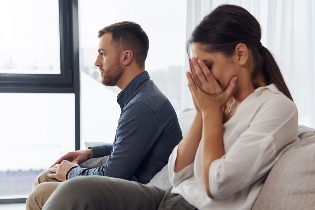 ソファーに座る男性と、その隣で顔を覆っている女性